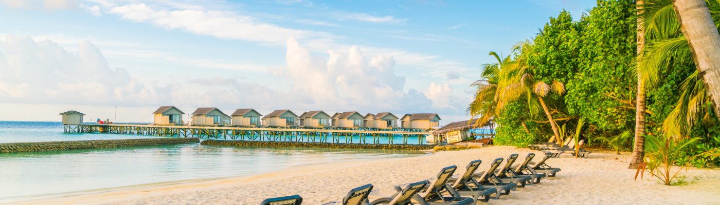 Beach chairs in Maldives island with water villas at the sunrise time